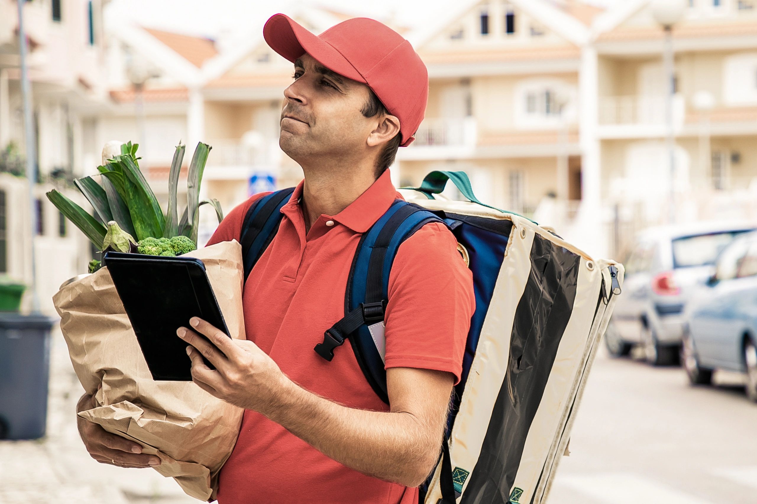 Courier with insulated delivery backpack checking a tablet before a delivery